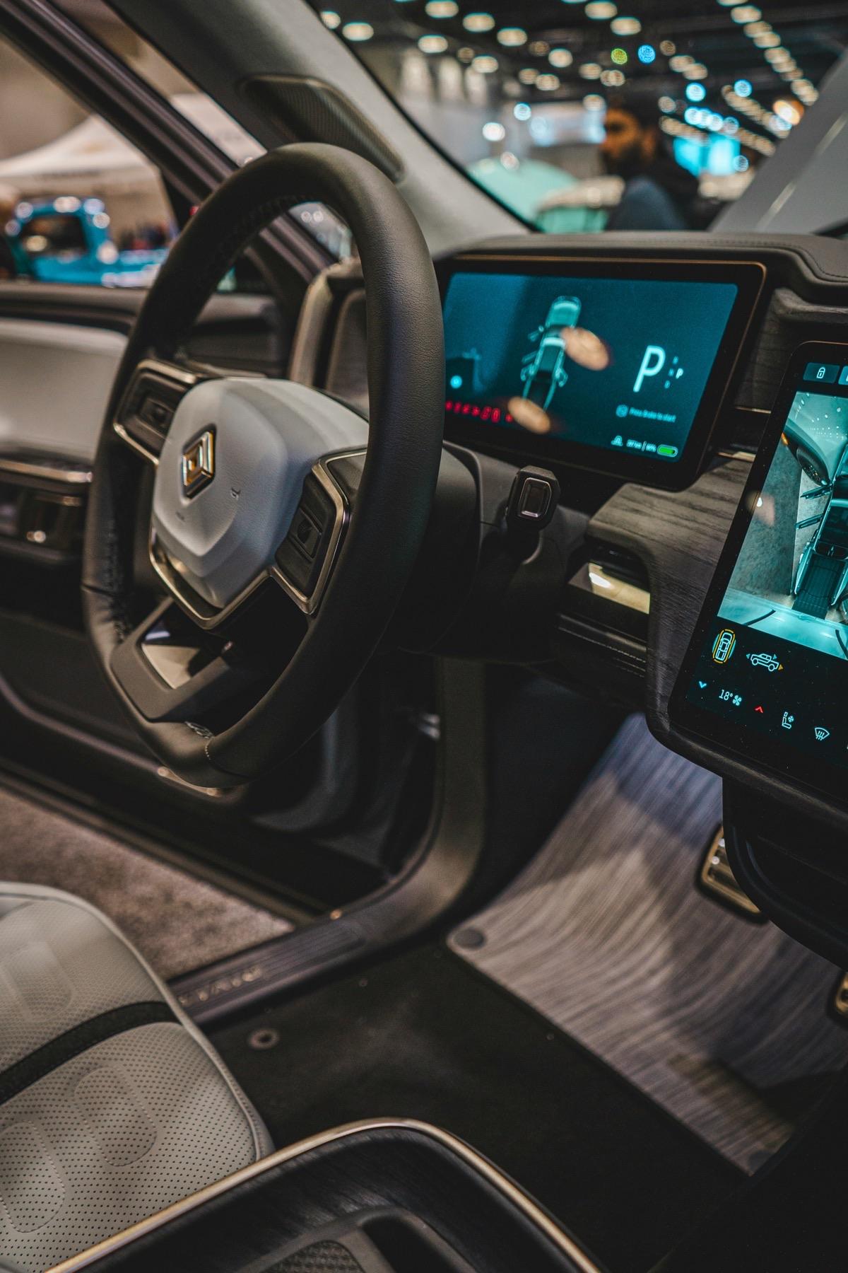 Rivian interior showing steering wheel, dual screens, and wood trim